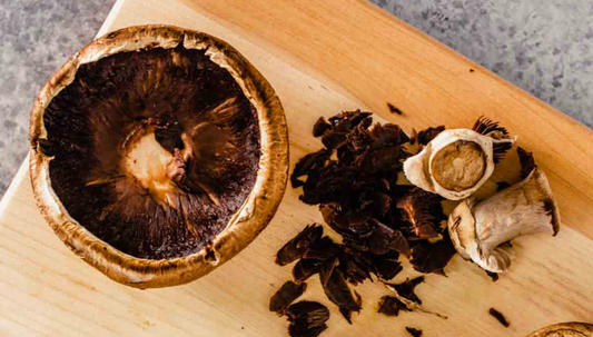 A large portobello mushroom cap on a wooden cutting board next to removed dark gills and trimmed stems.