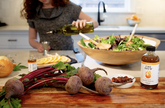 Woman preparing salad with fresh beets, citrus slices, and Fire Brew tonic in a modern kitchen.