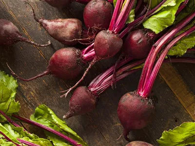Freshly harvested raw beetroots with vibrant green leaves and reddish-purple roots, laid out on a rustic wooden surface.