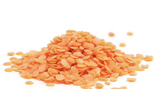 A pile of dry red lentils scattered on a white surface with some individual lentils spread around.
