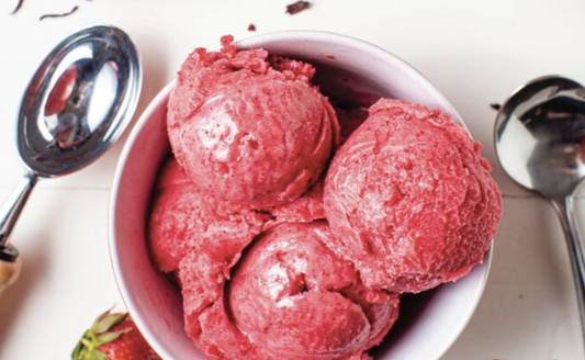 Four scoops of bright pink strawberry hibiscus sorbet in a white bowl with a scooper on the side.