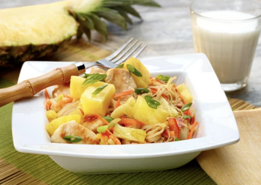 Colorful stir-fry with chicken, pineapple chunks, and veggies served over noodles in a white square bowl.