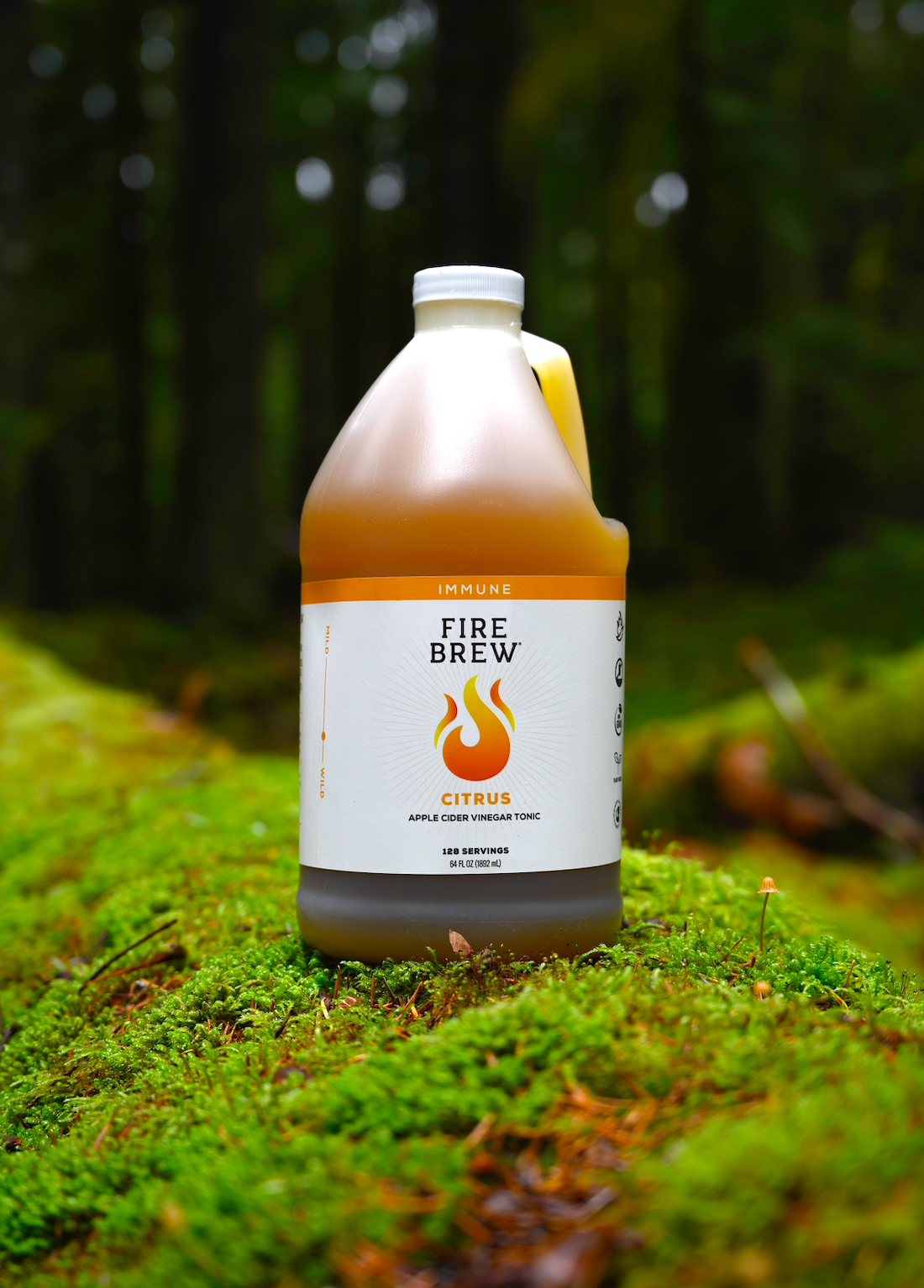 A Fire Brew Citrus Apple Cider Vinegar Tonic bottle sits on a vivid green mossy forest floor.