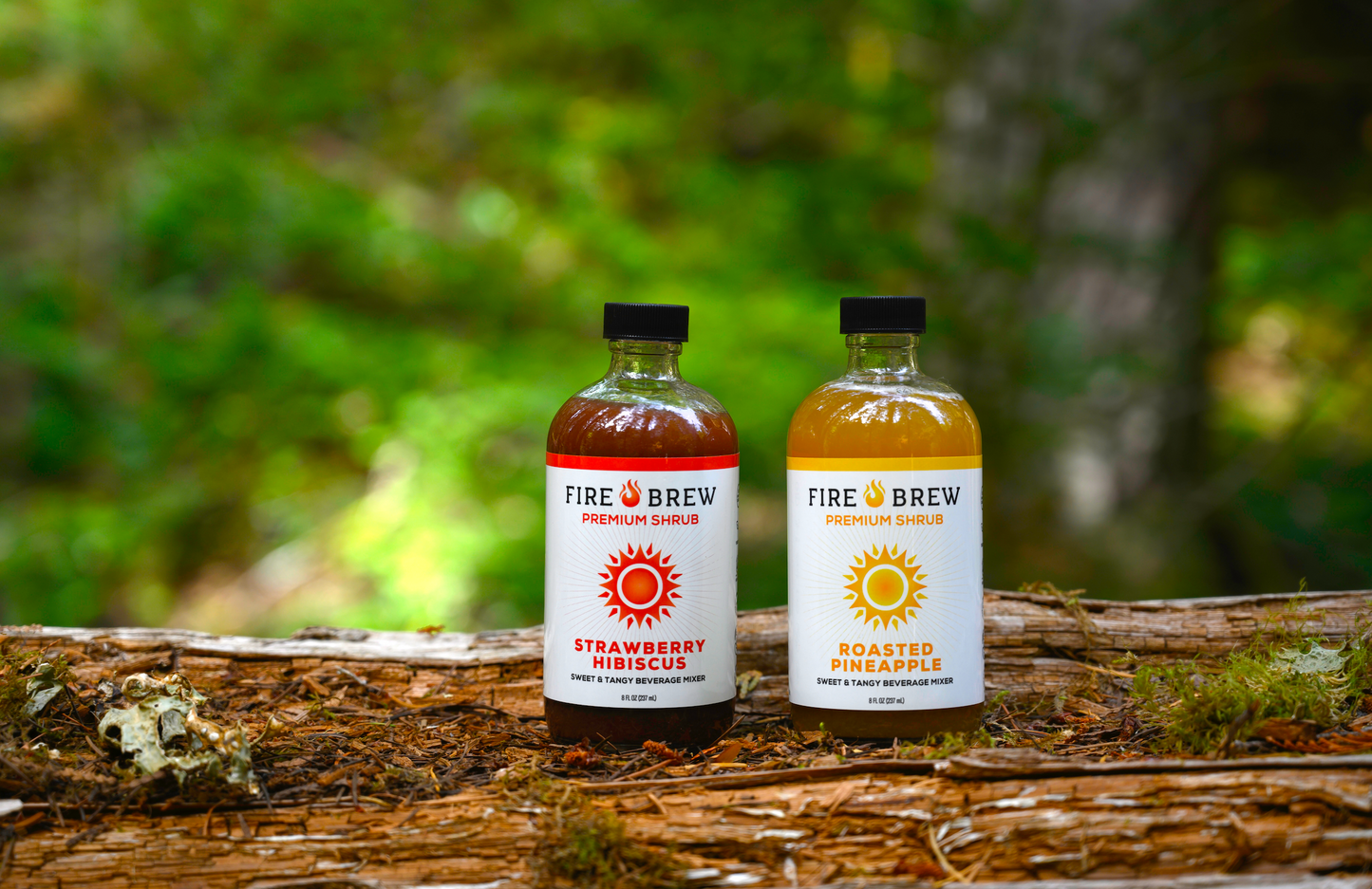 Fire Brew Strawberry Hibiscus and Roasted Pineapple Apple Cider Vinegar shrubs on a mossy log in the forest.