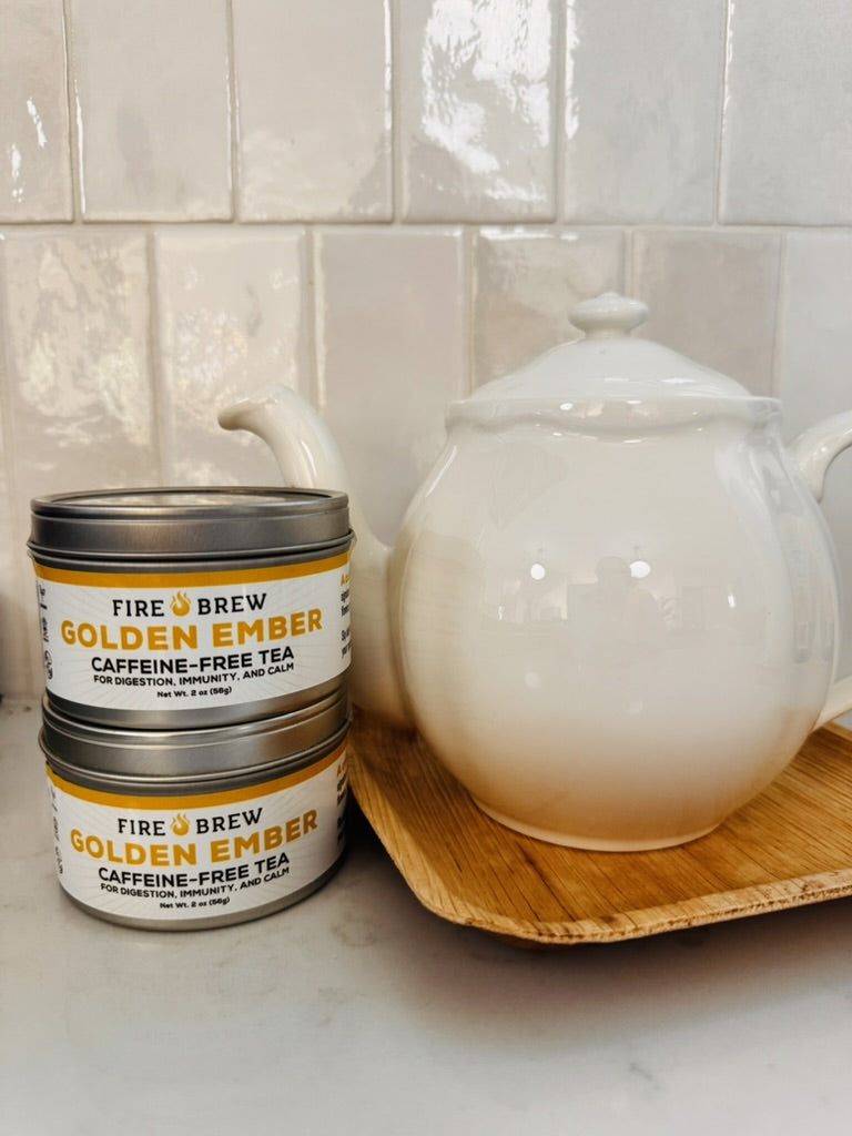 Fire Brew Golden Ember caffeine-free tea tins with white teapot on tray for calm herbal tea.