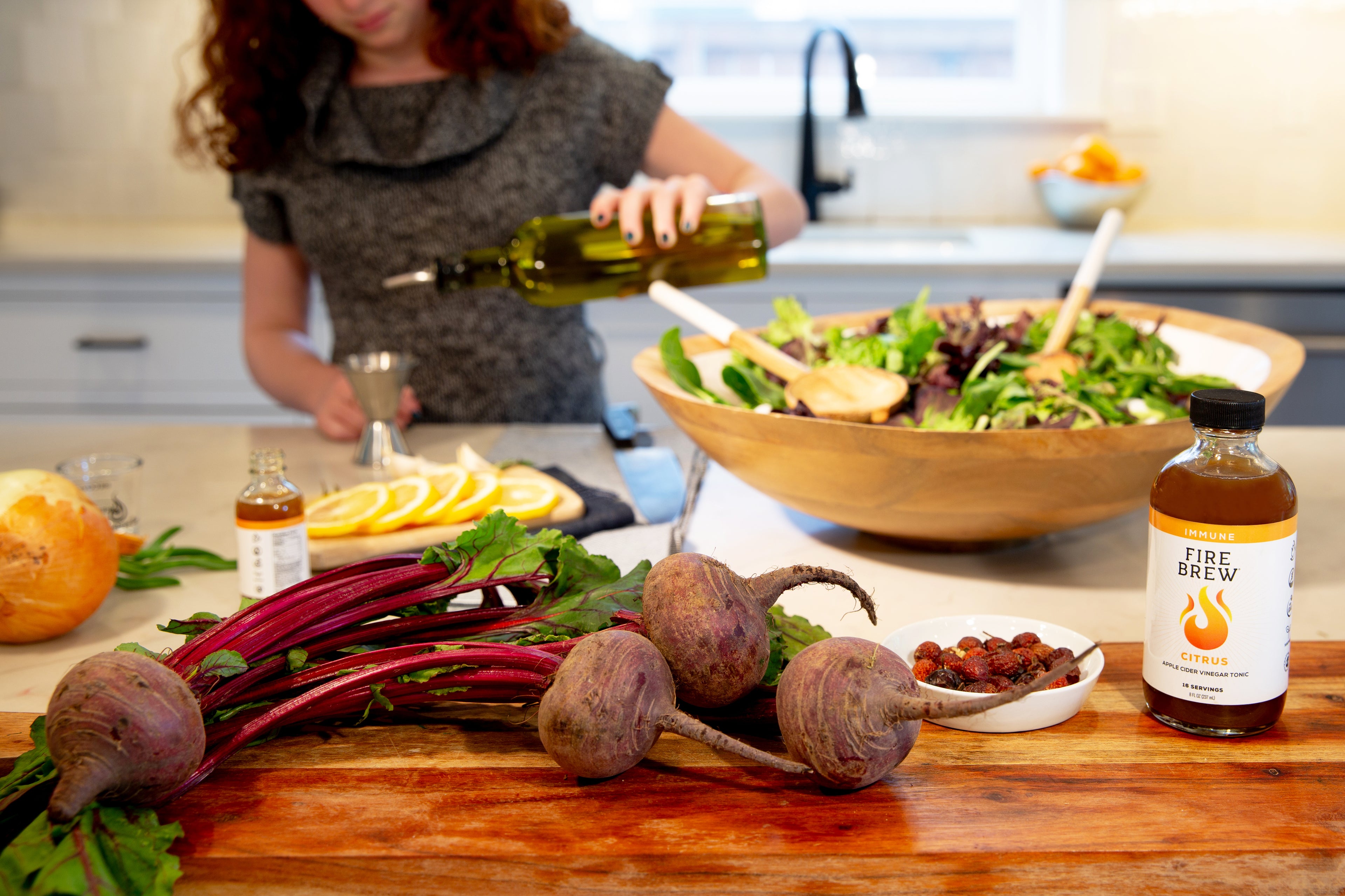Woman prepping salad with beets, citrus, and Fire Brew Apple Cider Vinegar tonic on a bright kitchen counter.