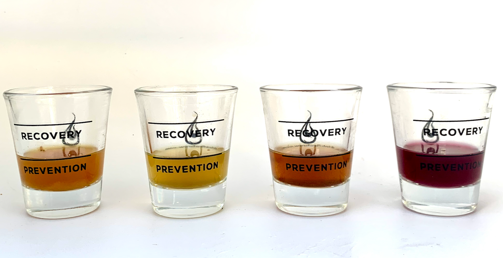 Four Fire Brew shot glasses filled with different colored tonics labeled Recovery and Prevention.