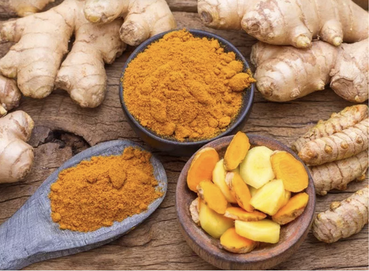 Fresh ginger roots, sliced turmeric, and vibrant turmeric powder displayed on a rustic wooden surface.