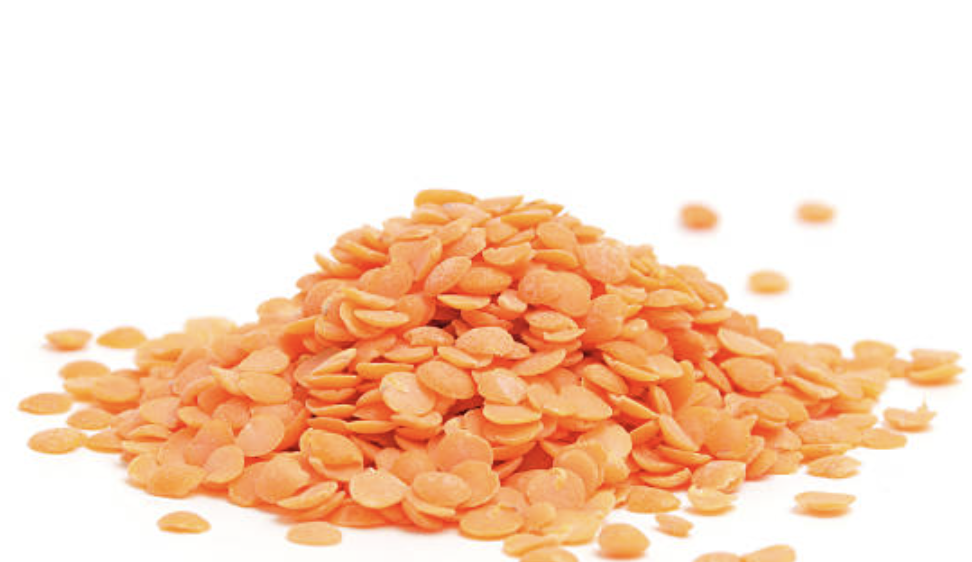 A pile of dry red lentils scattered on a white surface with some individual lentils spread around.