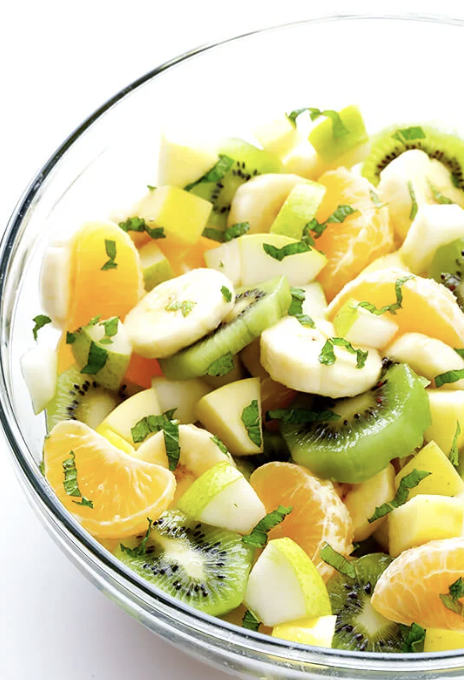 Fresh fruit salad with bananas, kiwis, oranges, apples, and mint for a vibrant and healthy treat.
