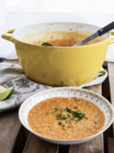 Creamy orange lentil soup served in a white bowl, with a yellow pot and ladle in the background on a rustic table.