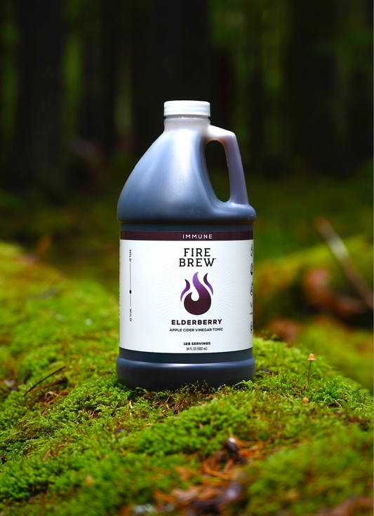 A bottle of Fire Brew Elderberry Apple Cider Vinegar Tonic stands on a lush green moss-covered forest floor.
