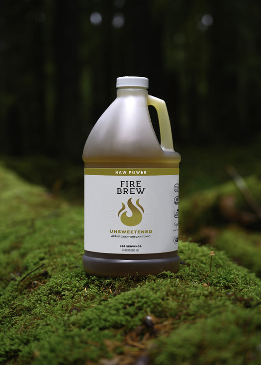Fire Brew Raw Power unsweetened apple cider vinegar tonic jug on lush forest moss, 64 fl oz bottle.