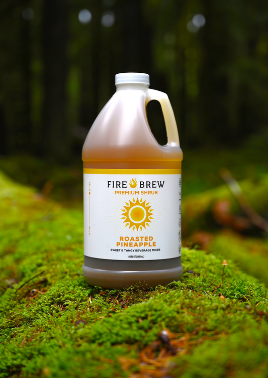 Fire Brew Roasted Pineapple apple cider vinegar shrub bottle on mossy forest floor, glowing with golden tones.