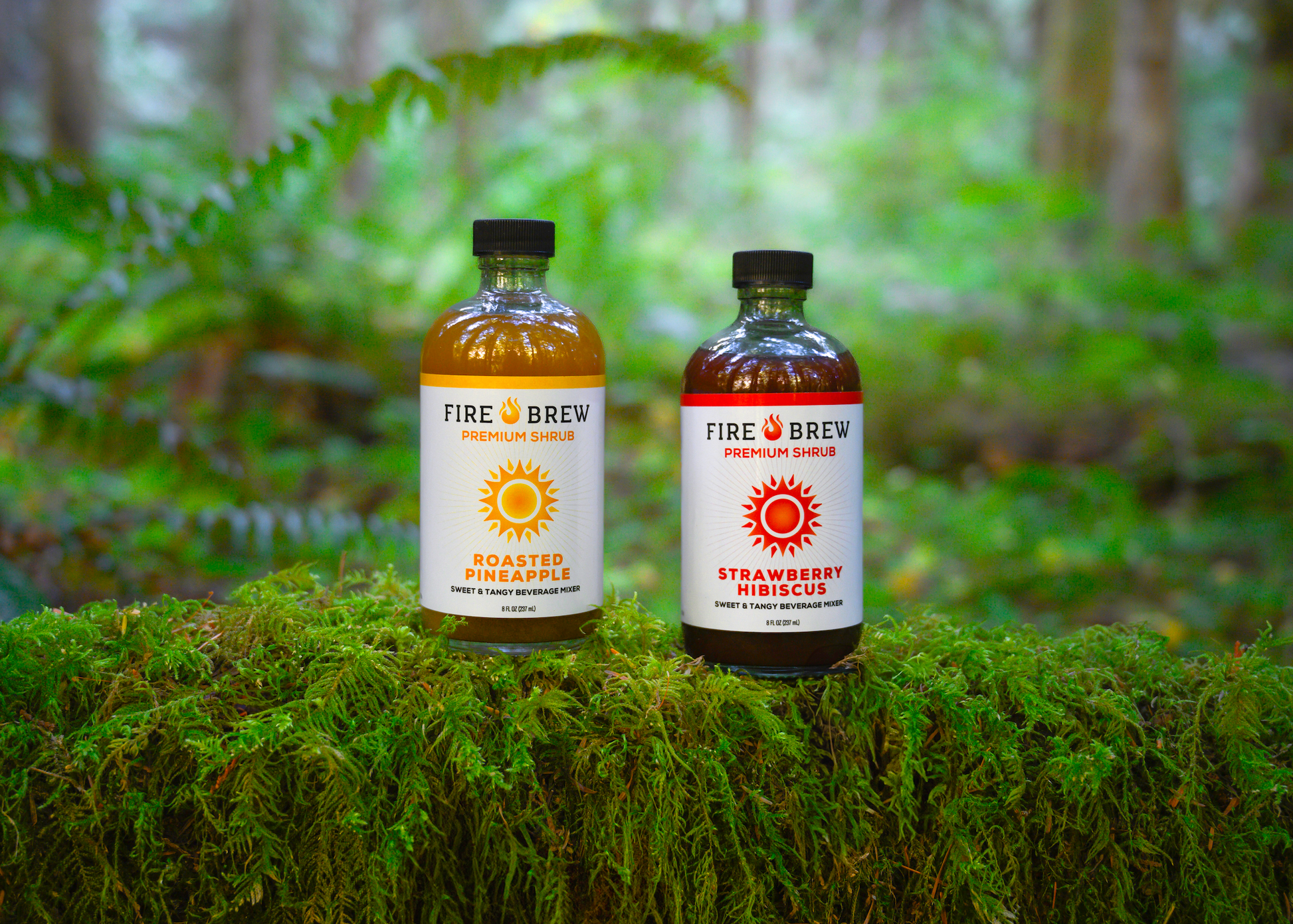 Fire Brew Roasted Pineapple and Strawberry Hibiscus Apple Cider Vinegar shrubs on green moss in a forest.
